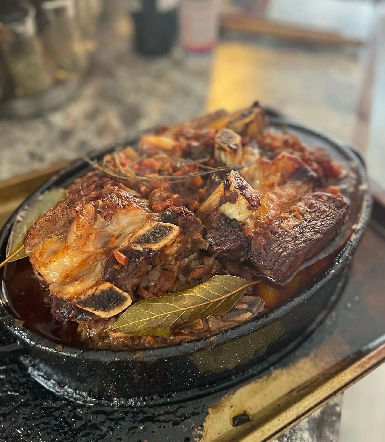 Braised bone-in short ribs with bay leaves in a cast iron pan