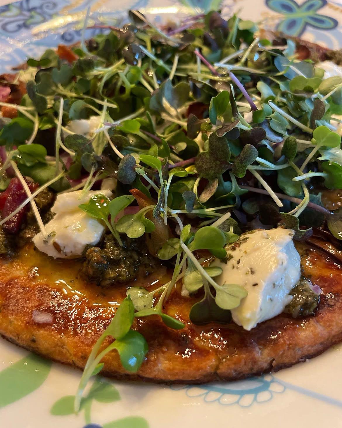 A flatbread topped with pesto, soft cheese and fresh microgreens
