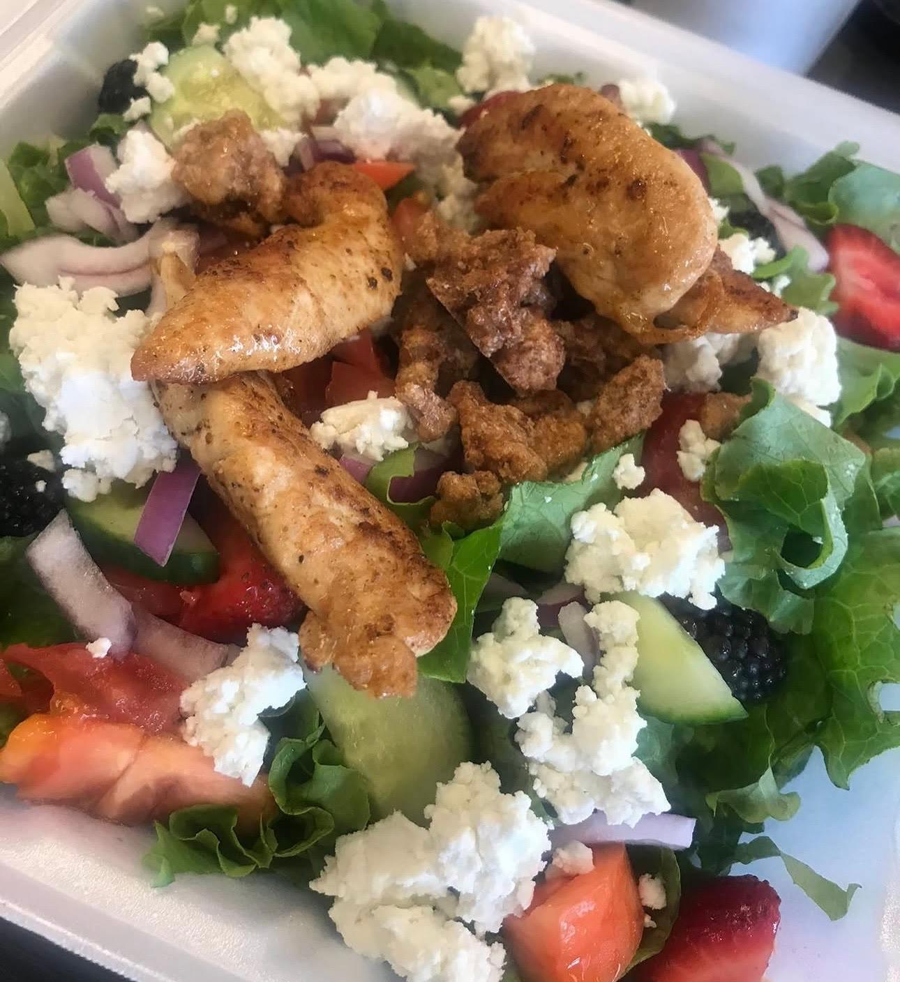 Sliced chicken over greens with crumbled white cheese, strawberries, blackberries, cucumber and red onion